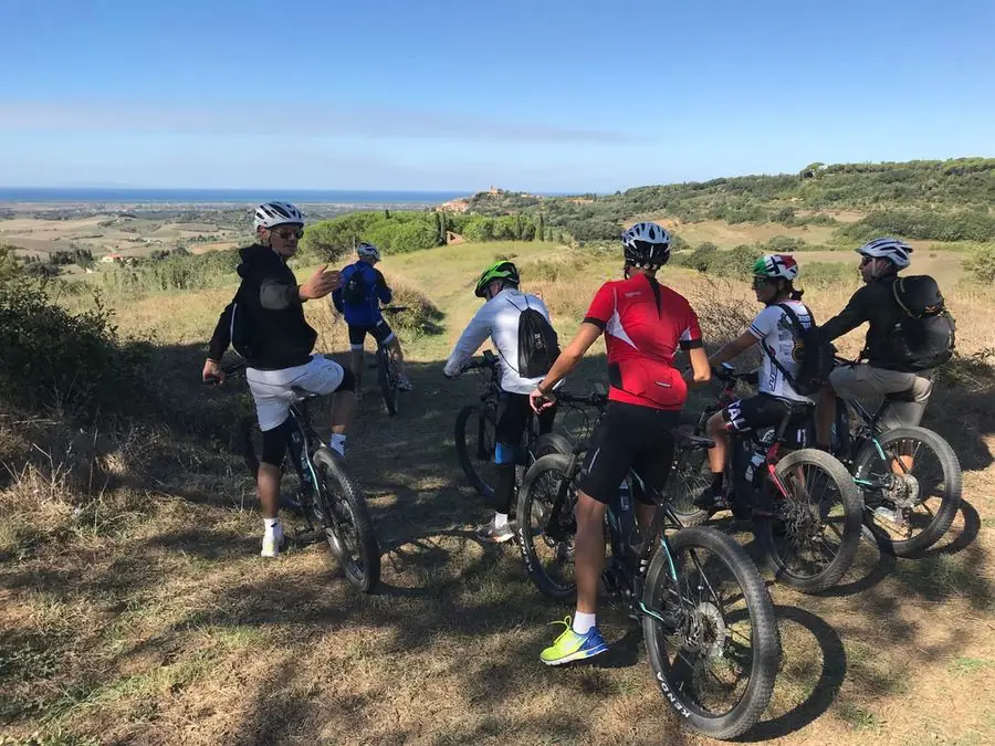 Group riding e-bikes past a stone church tower on a Tuscan hillside