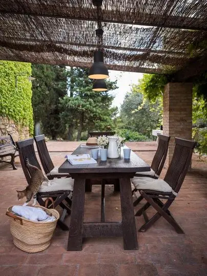 A long wooden table set for lunch beneath the villa's pergola